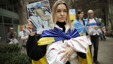 متظاهر يحمل دمية لطفل وصورة أثناء احتجاج الأم لدعم أوكرانيا في مقر اليونيسف في نيويورك ، في 19 آذار 2022 (أ ف ب).
