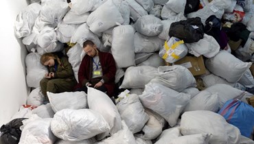 متطوعون في مركز إنساني يستريحون بين أكياس الملابس التي تم التبرع بها لمن تم إجلاؤهم، في مدينة لفيف غرب أوكرانيا (19 آذار 2022، أ ف ب). 