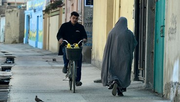 رجل على دراجة يمر قرب امرأة تسير في شارع في كابول (19 آذار 2022، أ ف ب). 