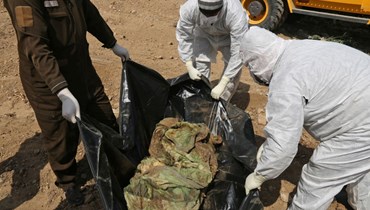 عاملون في الطب الشرعي العراقي يفحصون رفاتا عثر عليه في مقبرة جماعية في الموصل شمال العراق (20 آذار 2022ـ أ ف ب). 