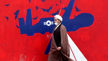 رجل دين إيراني يمر قرب جدارية مناهضة للولايات المتحدة على جدار المقر السابق للسفارة الاميركية في طهران (12 آذار 2022، أ ف ب). 