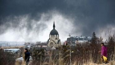 أشخاص يمرون قبالة كنيسة بينما تصاعد الدخان بعد غارة جوية في مدينة لفيف غرب أوكرانيا (26 آذار 2022، ا ف ب). 