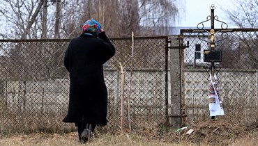 امرأة ترسم اشارة الصليب عند موقع مقبرة جماعية في بلدة بوروديانكا شمال غرب كييف (4 نيسان 2022، أ ف ب). 