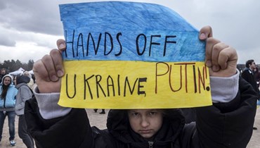 صبي حمل لافتة كُتب عليها "بوتين، ارفع يدك عن أوكرانيا" خلال الحفلة الموسيقية الخيرية "معًا من أجل أوكرانيا" في براغ (3 نيسان 2022، أ ف ب). 