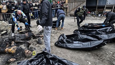 رجال الشرطة وعمال المدينة يحملون ست جثث محترقة جزئيًا في أكياس الجثث أثناء حضور المراسلين الصحافيين في بلدة بوتشا في 5 نيسان 2022 (أ ف ب).