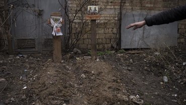 شخص يشير بيده الى قبرين لمدنيّين مدفونين في فناء خلفي في بوتشا بضواحي كييف (6 نيسان 2022، أ ب). 