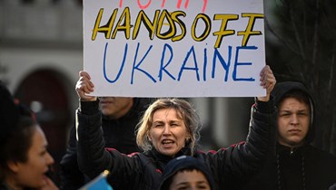 امرأة تحمل لافتة كتب عليها "بوتين ارفع يدك عن أوكرانيا" خلال احتجاج على الغزو الروسي لأوكرانيا أمام السفارة الروسية في بوخارست (3 نيسان 2022، أ ف ب). 