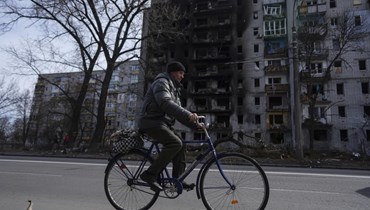 رجل يمر بدراجته قرب مبنى سكني متضرر من جراء القصف الروسي على مشارف تشيرنيهيف بأوكرانيا (7 نيسان 2022، أ ب). 