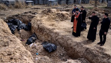 كهنة يصلون امام أكياس جثث في مقبرة جماعية في الحديقة المحيطة بكنيسة القديس أندرو في بوتشا بأوكرانيا (7 نيسان 2022، أ ف ب). 