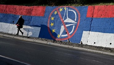 شخص يمر قرب جدارية مناهضة للاتحاد الأوروبي وحلف شمال الأطلسي في بلغراد قبل يوم من الانتخابات العامة والرئاسية في صربيا (2 نيسان 2022، أ ف ب). 