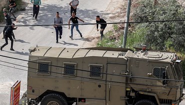 فلسطينيون يرشقون سيارة عسكرية إسرائيلية بالحجارة خلال مواجهات في مخيم جنين للاجئين الفلسطينيين في الضفة (9 نيسان 2022، أ ف ب). 