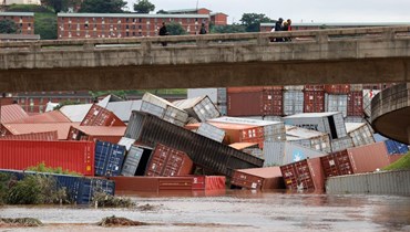 سكان من بلدة أوملازي وقفوا على جسر لرؤية حاويات سقطت بعد هطول أمطار غزيرة في ديربان (12 نيسان 2022، أ ف ب). 
