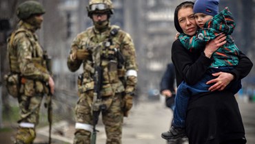 امرأة تحمل طفلًا خلال مرورها قرب جنود روس في أحد شوارع ماريوبول (12 نيسان 2022، أ ف ب). 