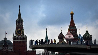 اشخاص يمشون على جسر في متنزه زاريادي في وسط موسكو، وفي الخلفية بدا برج سباسكايا بالكرملين وكاتدرائية القديس باسيل (4 ت2 2021، ا ف ب). 