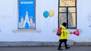 طفل يمشي بالقرب من كتابات رسمها الفنان فلاديمير أوفشينيكوف في بوروفسك ، على بعد حوالي 100 كيلومتر جنوب غرب موسكو ، في 14 نيسان 2022 (أ ف ب).