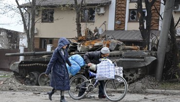 مدنيان يمران قرب دبابة مدمرة في ماريوبول (19 نيسان 2022، أ ب). 