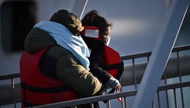 صورة تعبيرية- رجل يحمل طفلاً بين ذراعيه بعد نزوله مع مجموعة من المهاجرين من قارب لحرس الحدود في مارينا دوفر في دوفر في الساحل الجنوبي الشرقي لإنكلترا (18 نيسان 2022، أ ف ب). 