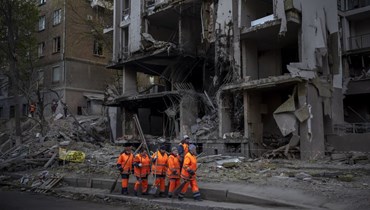 عمال تنظيف يستعدون للعمل في موقع انفجار في كييف بأوكرانيا (29 نيسان 2022، أ ب). 
