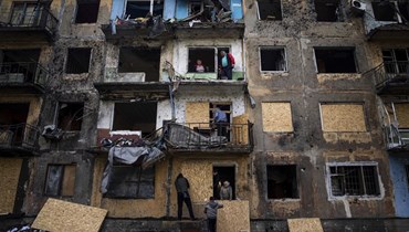 سكان يغلقون نوافذ مبنى سكني بقطع من الخشب بعد قصف روسي في دوبروبيليا بمنطقة دونيتسك شرق أوكرانيا (30 نيسان 2022، أ ب). 