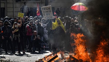 متظاهرون تجمّعوا قرب حريق أُشعل على طريق في باريس خلال اشتباكات مع الشرطة اثناء احتجاجات عيد العمال (1 ايار 2022، أ ف ب). 