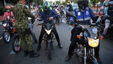 شرطي يدقّق في أوراق سائقي سيارات عند نقطة تفتيش في مانيلا (8 ايار 2022، ا ف ب). 