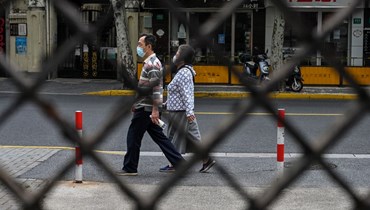 شخصان يمشيان في شارع في حي جينغان في شنغهاي خلال الإغلاق المفروض للحد من انتشار كورونا (19 ايار 2022، أ ف ب). 