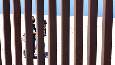 مهاجرون يمرون عند الجانب المكسيكي من الجدار الحدودي مع الولايات المتحدة (16 ايار 2022، أ ف ب). 