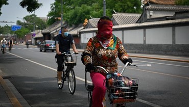 امرأة تقود دراجتها في بيجينغ، بينما غطت وجهها بوشاح (24 ايار 2022، أ ف ب). 