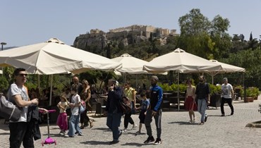 أشخاص يمشون في شارع عند سفح تل الأكروبوليس في أثينا (1 ايار 2022، أ ب). 