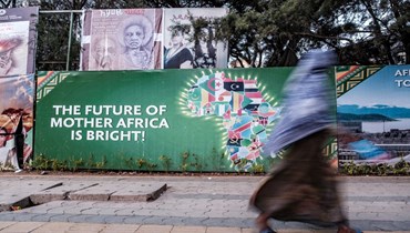 امرأة تمرّ قرب لافتة في أديس أبابا كانت في الأصل جزءًا من استعدادات المدينة لاستضافة القمة الـ35  للاتحاد الأفريقي في شباط 2022 (24 ايار 2022، أ ف ب). 