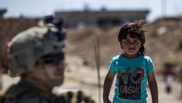 طفل سوري إلى جانب أحد أفراد القوات الأميركية في ريف الرميلان في الحسكة بالقرب من الحدود التركية (أ ف ب).