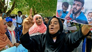 سودانيون يرفعون لافتات خلال تجمعهم خارج محكمة في الخرطوم دعما للمتظاهرين المتهمين بقتل ضابط شرطة (29 ايار 2022، أ ف ب). 