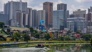 قارب يشق طريقه في مياه نهر باسيج قبالة ابنية شاهقة في منطقة ماكاتي التجارية في مانيلا (29 ايار 2022، أ ف ب). 