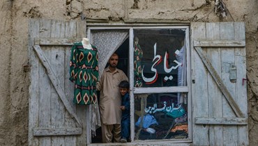 خياط، قربه طفل، يطل من واجهة متجره في كابول (2 حزيران 2022، أ ف ب). 