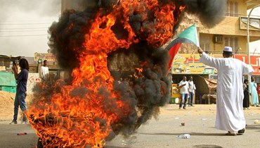 سوداني يلوح بالعلم الوطني قرب إطارات مشتعلة في الخرطوم خلال تظاهرة للمطالبة بالعدالة لعشرات المحتجين المؤيدين للديموقراطية الذين قُتلوا خلال قمع اعتصام 2019 ضد البشير (3 حزيران 2022، ا ف ب).