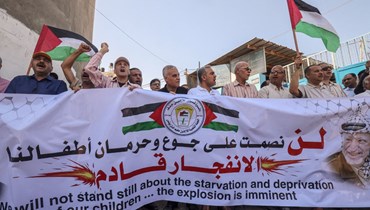 فلسطينيون رفعوا لافتة خلال تظاهرة خارج مكاتب "الأونروا" في مخيم خان يونس للاجئين جنوب قطاع غزة احتجاجًا على قطع المساعدات (14 حزيران 2022، أ ف ب). 
