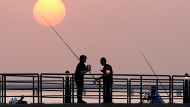 أشخاص يصطادون عند رصيف بحري في مدينة الكويت عند غروب الشمس (13 حزيران 2022، أ ف ب). 