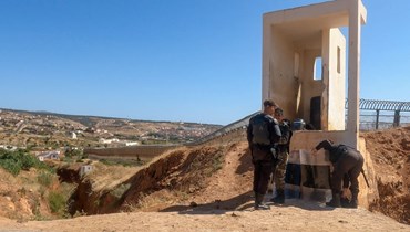 رجال أمن مغاربة وقفوا عند السياج الحدودي الفاصل بين المغرب (الى اليسار) وجيب مليلية الإسباني (إلى اليمين) قرب الناظور في المغرب (25 حزيران 2022، أ ف ب).