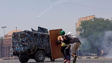 متظاهرون مناهضون للانقلاب يختبئون خلف درع خشبي في مواجهة ناقلة جند مدرعة تابعة لقوات الأمن خلال احتجاج في الخرطوم (30 حزيران 2022، أ ف ب).