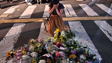 امرأة تبكي قرب باقات وضعت في مكان اطلاق النار على آبي خارج محطة ياماتو-سايداجي في نارا (8 تموز 2022، أ ف ب). 