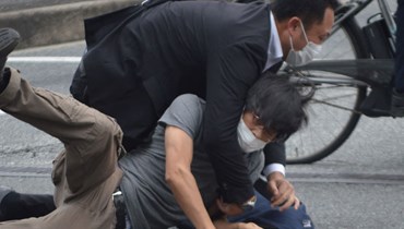 رجل (على الارض) يشتبه في انه مطلق النار على آبي يقبض عليه شرطي في محطة ياماتو سايداجي في مدينة نارا (8 تموز 2022، أ ف ب). 