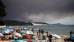 مستحمون يستلقون على شاطئ بيلا سور مير بينما ارتفعت سحابة سوداء من الدخان من جراء حريق أصاب غابة لا تيست دو باك، في أركاشون جنوب غرب فرنسا (13 تموز 2022، أ ف ب). 