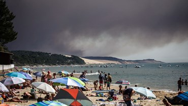 مستحمون يستلقون على شاطئ بيلا سور مير بينما ارتفعت سحابة سوداء من الدخان من جراء حريق أصاب غابة لا تيست دو باك، في أركاشون جنوب غرب فرنسا (13 تموز 2022، أ ف ب). 