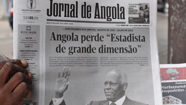 رجل يحمل نسخة من صحيفة "جورنال دي أنغولا" مع عنوان رئيسي حول وفاة رئيس أنغولا السابق خوسيه إدواردو دوس سانتوس في لواندا في 9 تموز 2022 (أ ف ب).