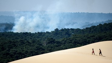 أشخاص يمشون على دون دو بيلات بينما تصاعد الدخان من جراء حريق غابة في لا تست دو باخ جنوب غرب فرنسا (16 تموز 2022، أ ف ب). 