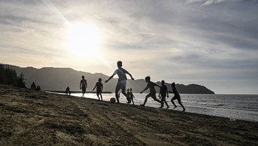  شبّان يلعبون كرة القدم على طول الساحل على الشاطئ الإندونيسي في 17 تموز 2022 (أ ف ب). 
