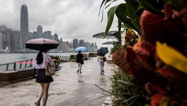 اشخاص يمشون تحت مظلات على كورنيش بجوار ميناء فيكتوريا في هونغ كونغ خلال يوم ماطر (12 آب 2022، أ ف ب). 