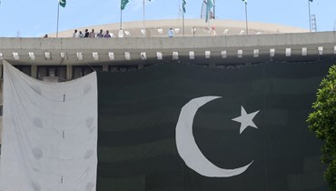 أشخاص يقفون فوق مبنى مزيّن بعلم كبير لباكستان في لاهور، قبل احتفالات بعيد استقلالها الـ75 (12 آب 2022، أ ف ب). 