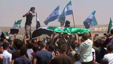 سوريون يلوحون بأعلام المعارضة خلال تظاهرة في قرية المسطومة جنوب إدلب (12 آب 2022، أ ف ب). 