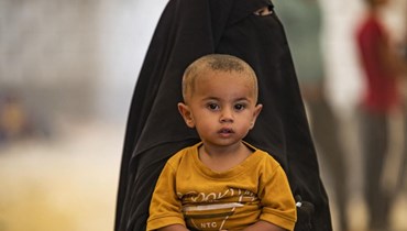 امرأة تحمل طفلها بينما ينتظر السوريون إطلاق سراحهم من مخيم الهول (أ ف ب).